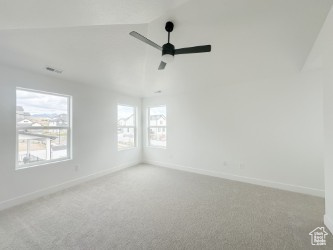 Empty room featuring ceiling fan, carpet, baseboards, and lofted ceiling
