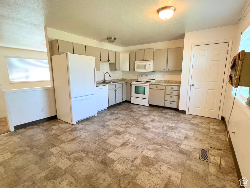 Kitchen with white appliances, baseboards, visible vents, light countertops, and a sink