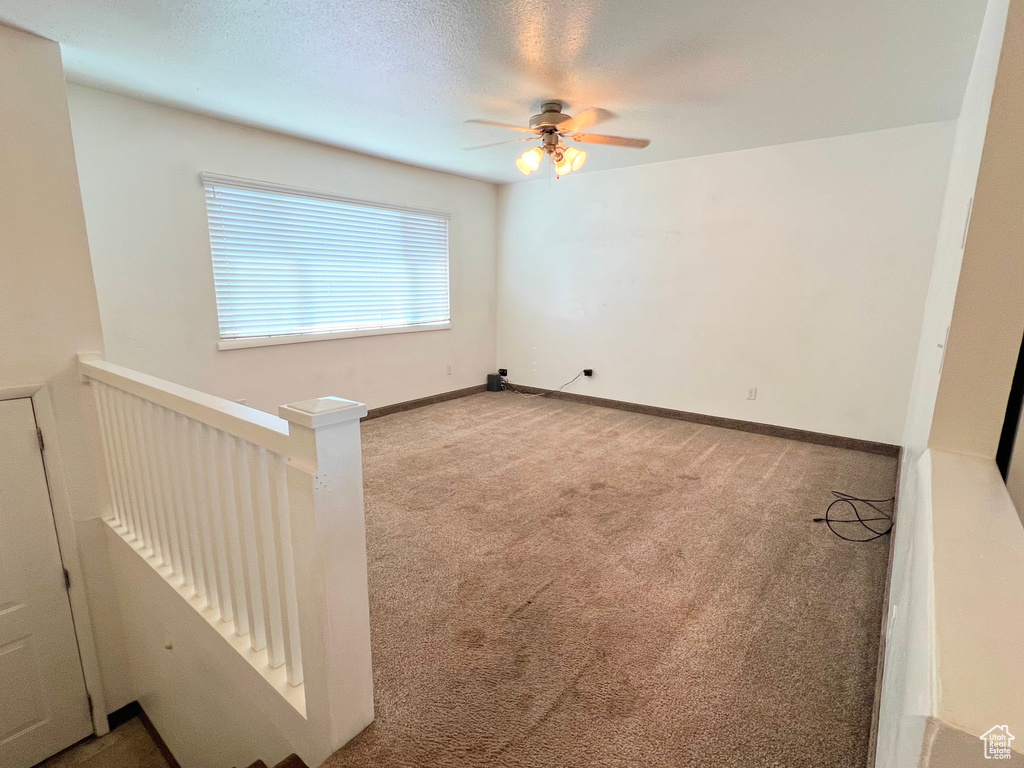 Empty room featuring a ceiling fan, light carpet, a textured ceiling, and baseboards