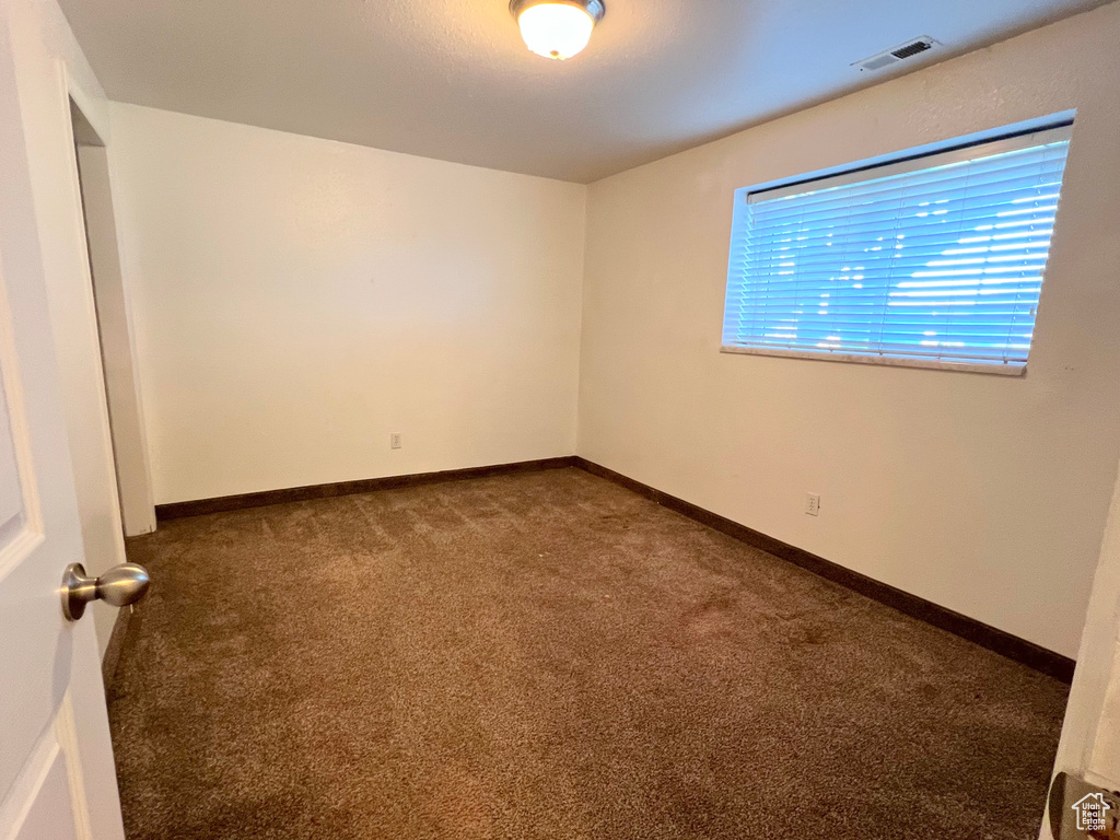 Empty room featuring dark carpet, visible vents, and baseboards
