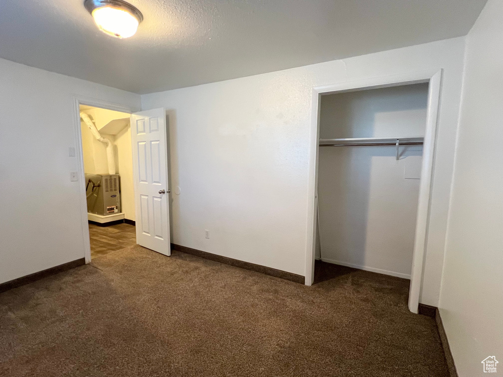 Unfurnished bedroom featuring dark colored carpet, a closet, and baseboards