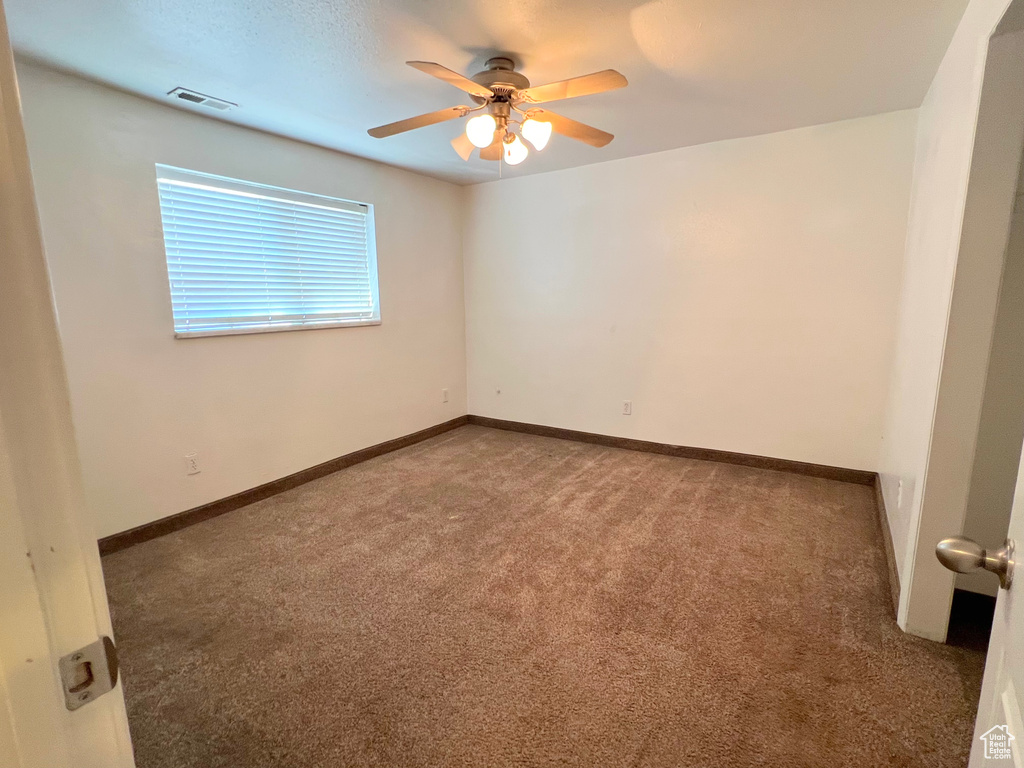Unfurnished room featuring a ceiling fan, dark carpet, visible vents, and baseboards