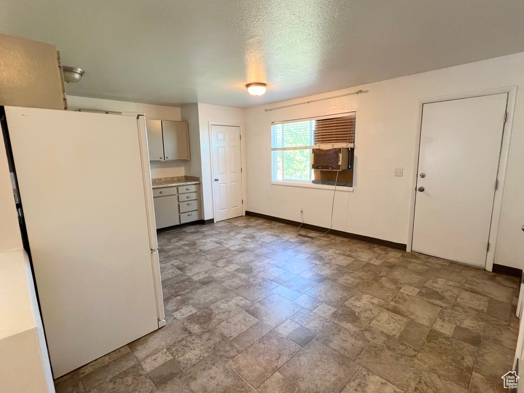 Kitchen featuring baseboards, freestanding refrigerator, stone finish flooring, light countertops, and a textured ceiling