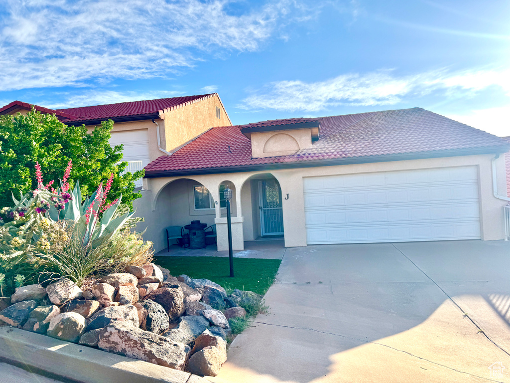 Mediterranean / spanish house featuring an attached garage, driveway, stucco siding, and a tile roof