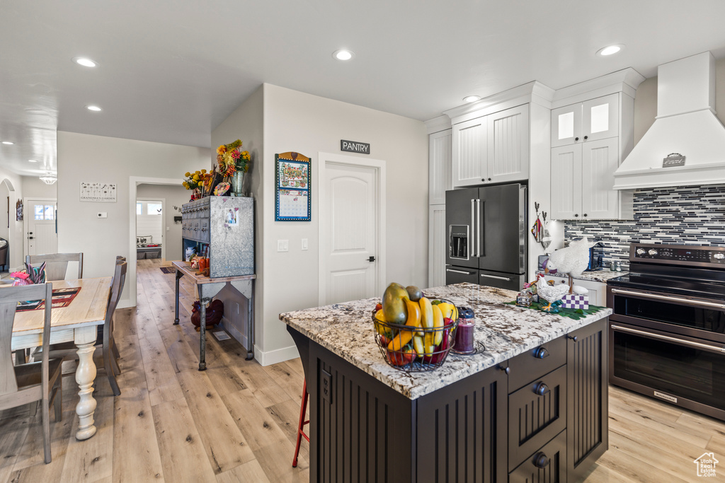 Kitchen featuring custom range hood, decorative backsplash, white cabinets, double oven range, and high end refrigerator