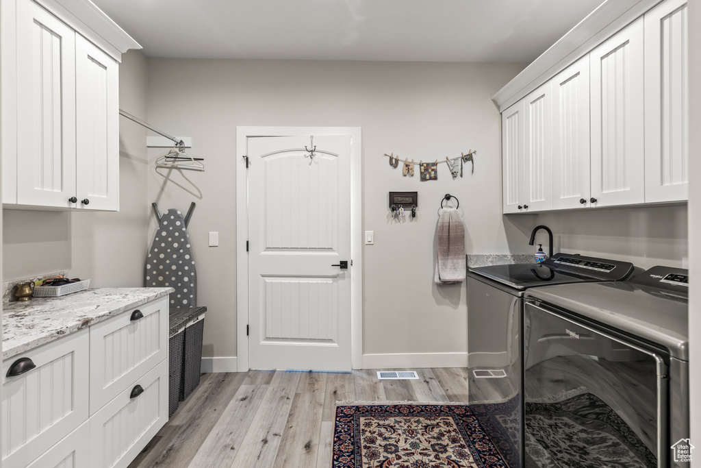 Laundry room featuring separate washer and dryer, visible vents, baseboards, light wood-type flooring, and cabinet space