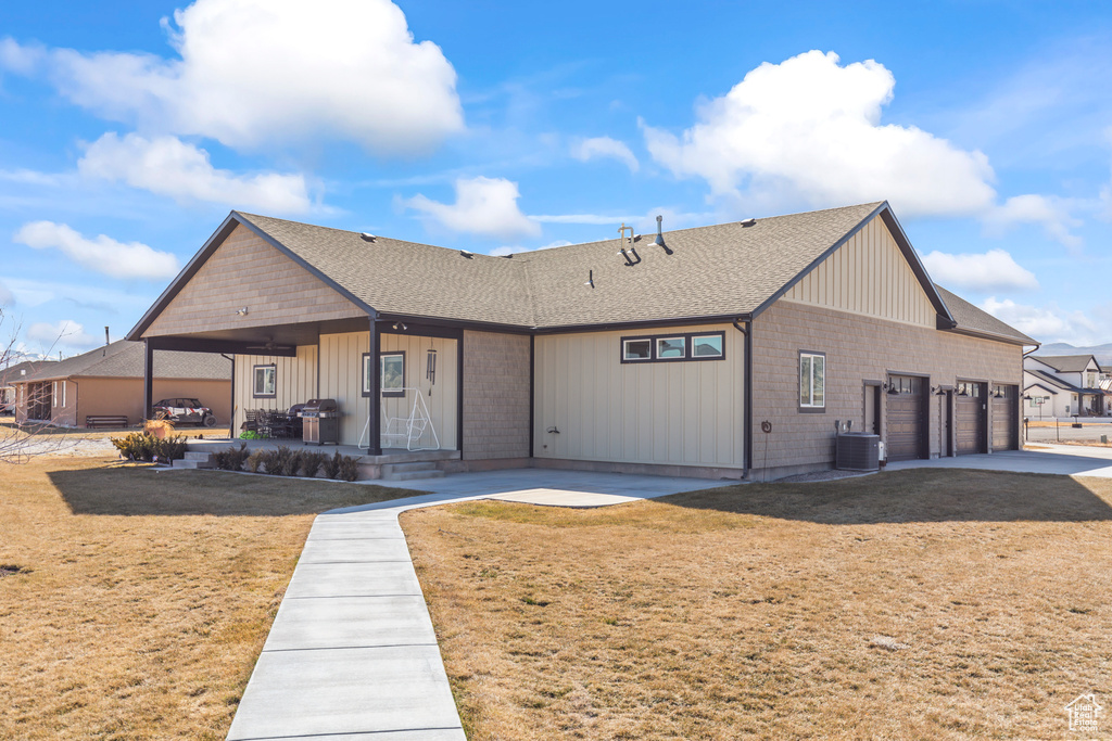 View of front of house featuring a front yard, a patio, an attached garage, and central AC unit