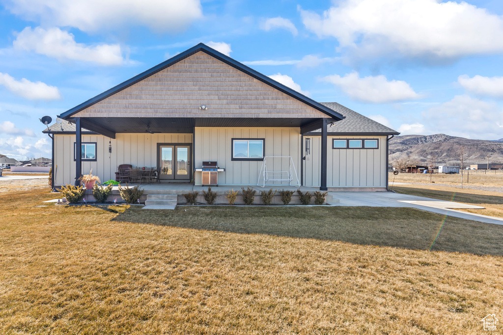 View of front facade with board and batten siding, french doors, a mountain view, and a front lawn
