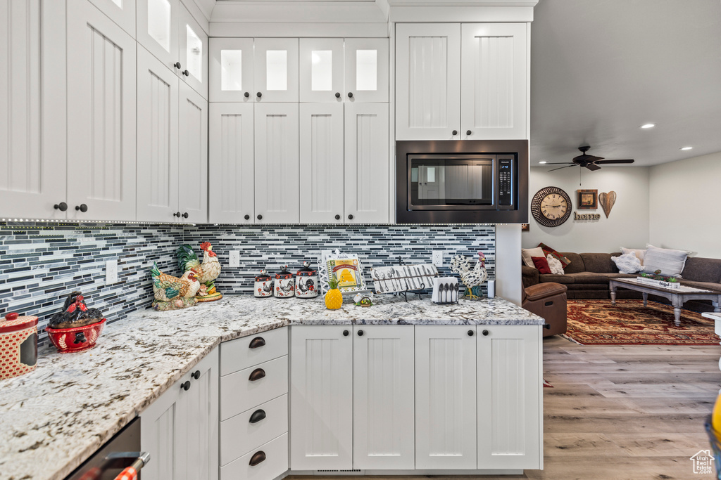 Kitchen with stainless steel microwave, backsplash, open floor plan, light stone countertops, and light wood-type flooring