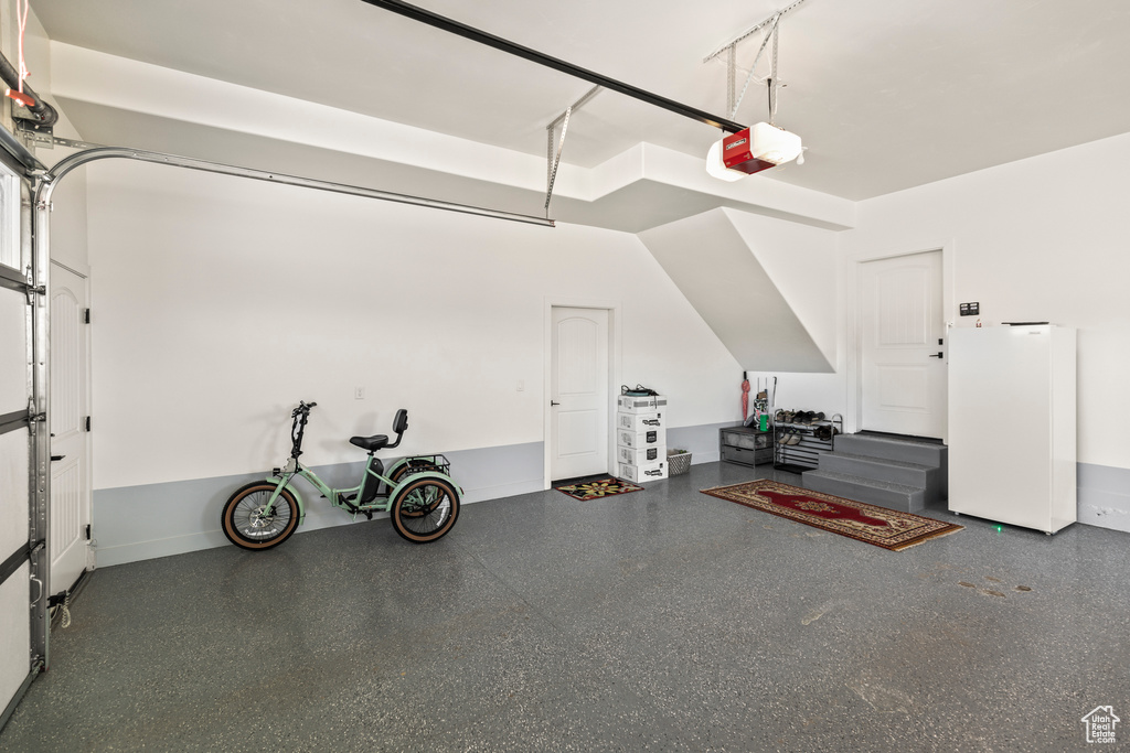 Garage featuring a garage door opener and freestanding refrigerator