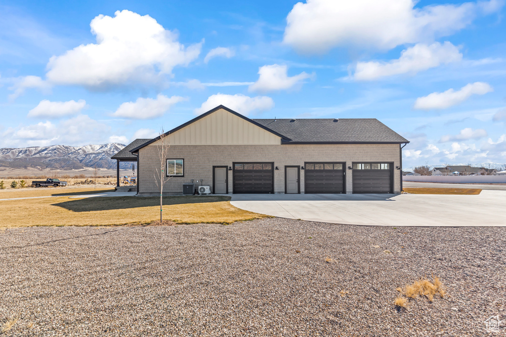 View of front of house with an attached garage, a mountain view, a shingled roof, concrete driveway, and a front lawn