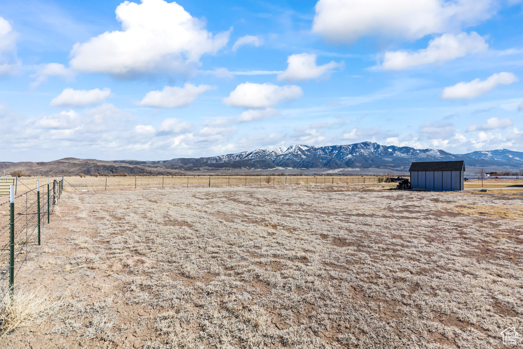 View of yard featuring a storage shed, a rural view, fence, an outdoor structure, and a mountain view