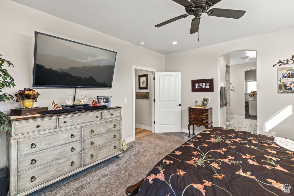 Carpeted bedroom featuring arched walkways, baseboards, ceiling fan, and ensuite bath