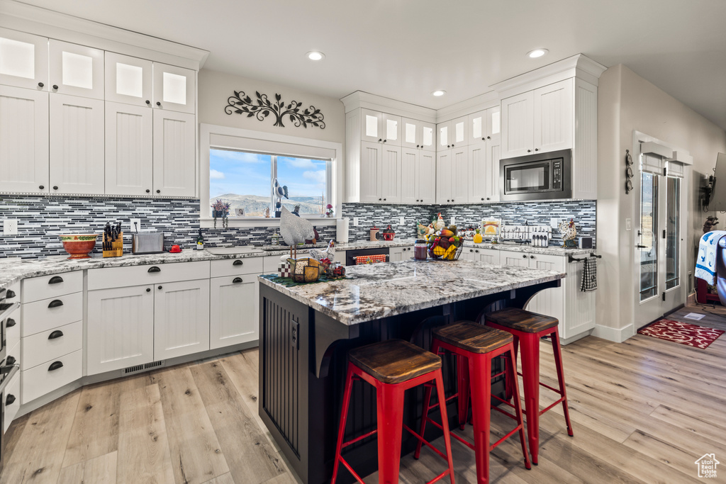 Kitchen with a breakfast bar area, light wood-style flooring, a kitchen island, white cabinetry, and built in microwave