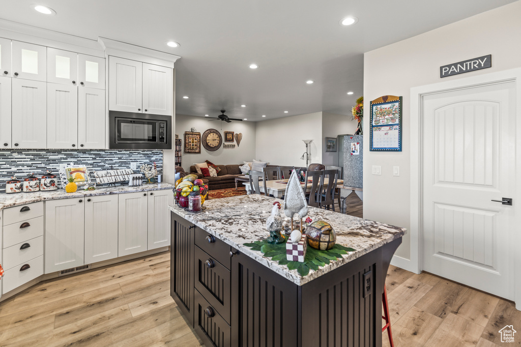 Kitchen featuring light wood finished floors, recessed lighting, white cabinetry, and built in microwave