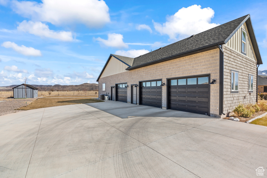 View of side of home featuring a shingled roof, concrete driveway, a mountain view, and central AC unit