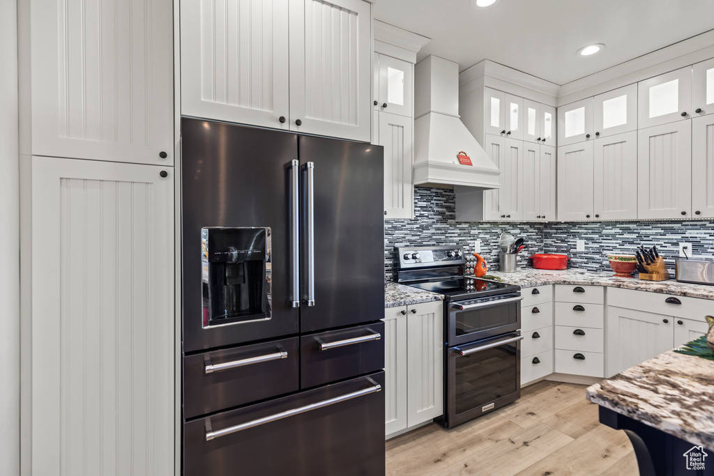 Kitchen with range with two ovens, premium range hood, high end refrigerator, white cabinets, and light wood finished floors