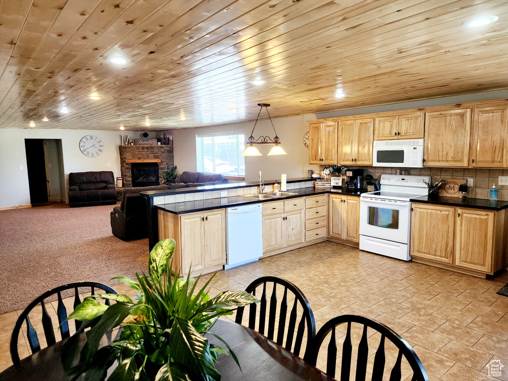 Kitchen with dark countertops, white appliances, pendant lighting, and open floor plan
