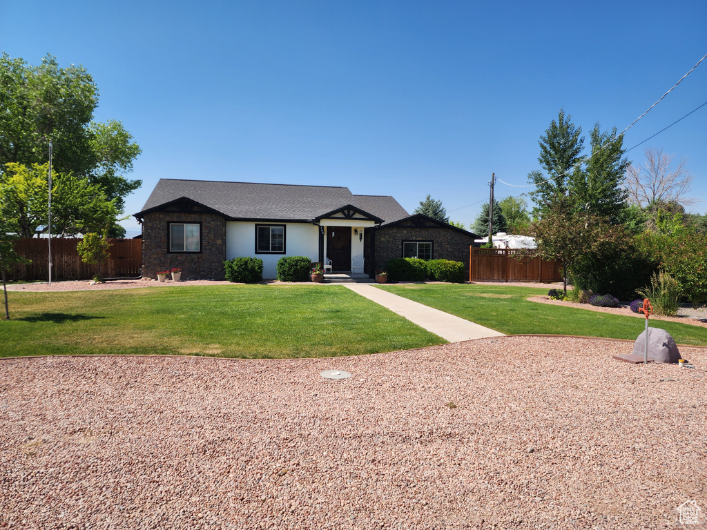 Single story home with stone siding, fence, and a front lawn