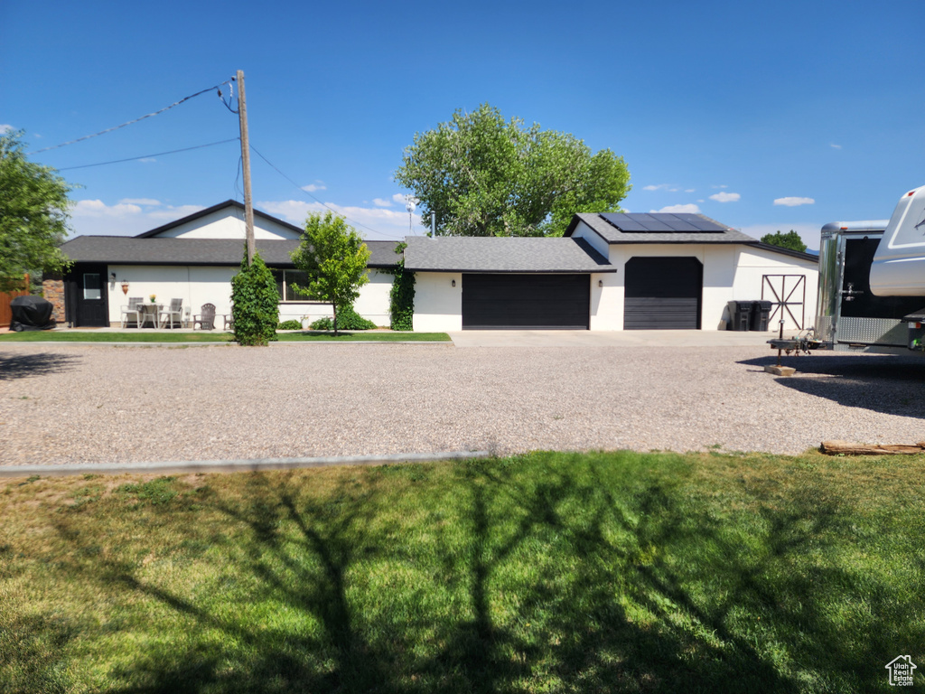 Single story home featuring an attached garage, a front yard, solar panels, and stucco siding