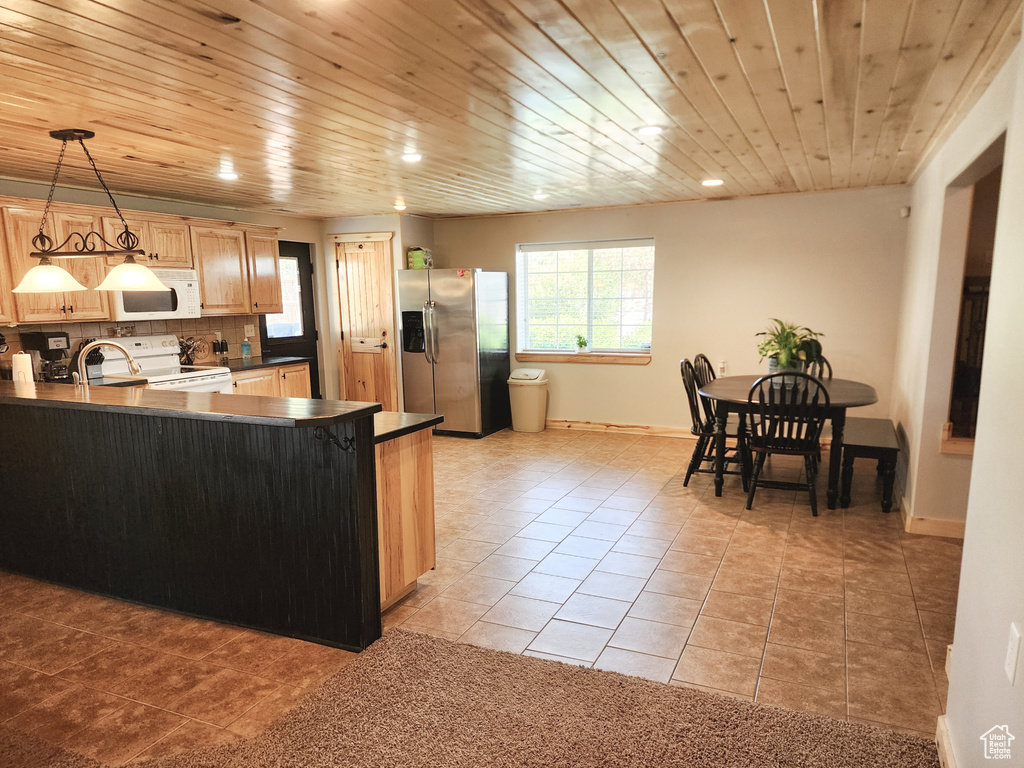 Kitchen with pendant lighting, dark countertops, white appliances, and a peninsula