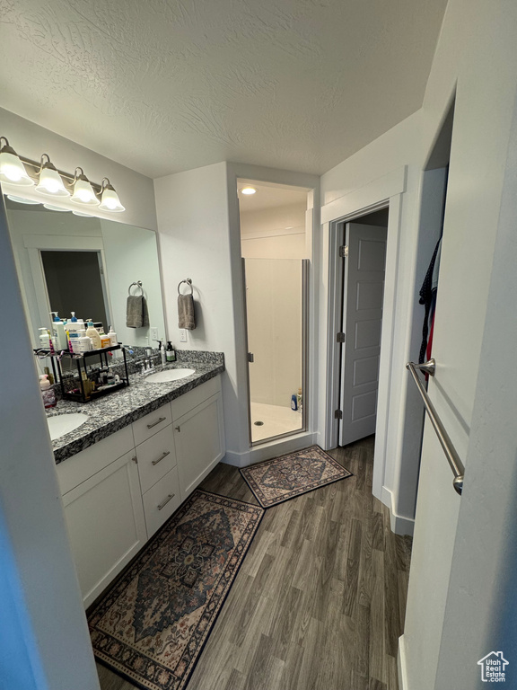 Bathroom with double vanity, a stall shower, wood finished floors, a textured ceiling, and a sink
