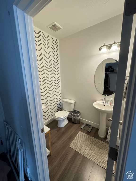 Bathroom featuring toilet, a sink, wood finished floors, visible vents, and baseboards