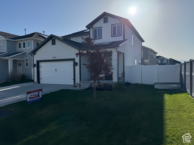 Traditional-style house featuring an attached garage, driveway, a front lawn, and fence