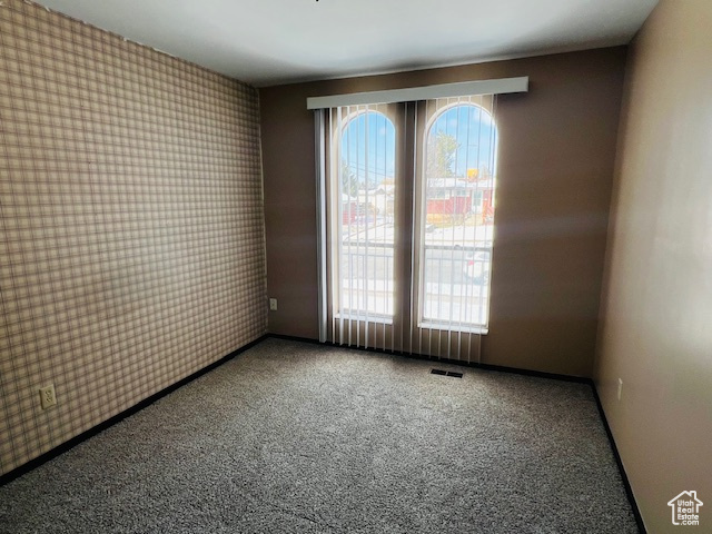 Unfurnished room featuring wallpapered walls, baseboards, visible vents, and carpet flooring