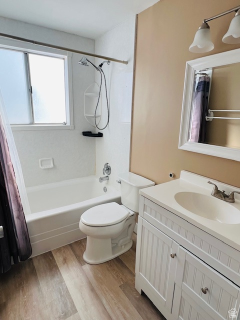 Bathroom with shower / bath combination with curtain, vanity, wood finished floors, and toilet