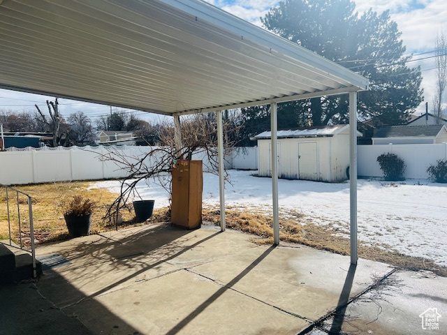 Snow covered patio with an outbuilding, a fenced backyard, and a shed