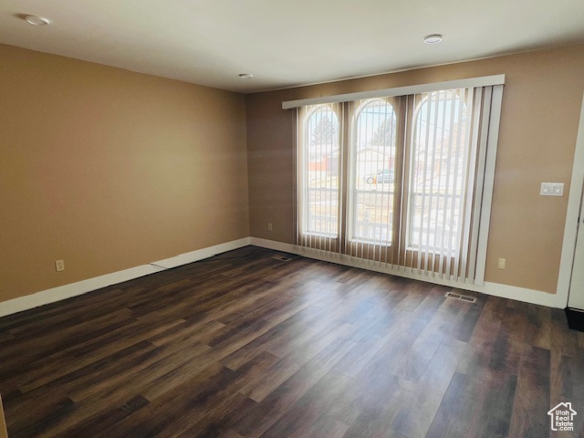 Unfurnished room with visible vents, dark wood finished floors, and baseboards