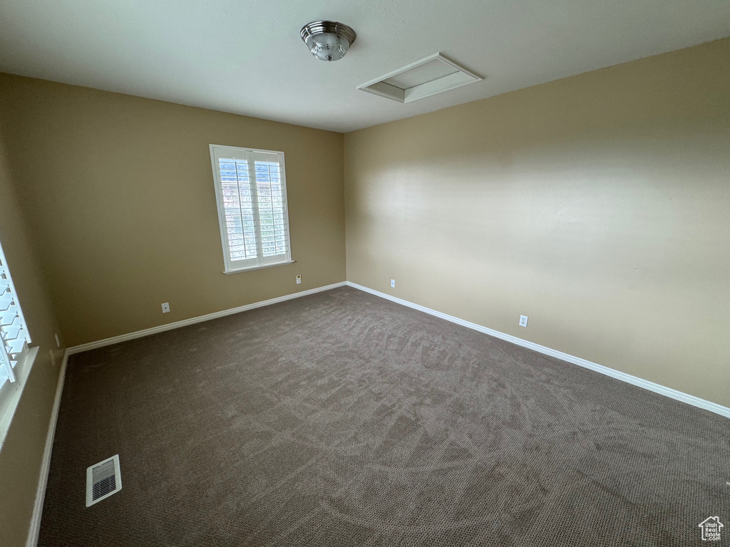 Spare room with baseboards, attic access, and dark carpet