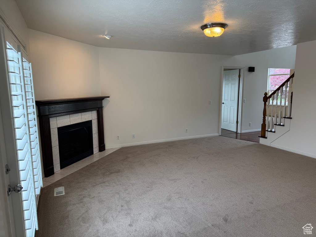 Unfurnished living room featuring carpet, a tiled fireplace, plenty of natural light, and stairs