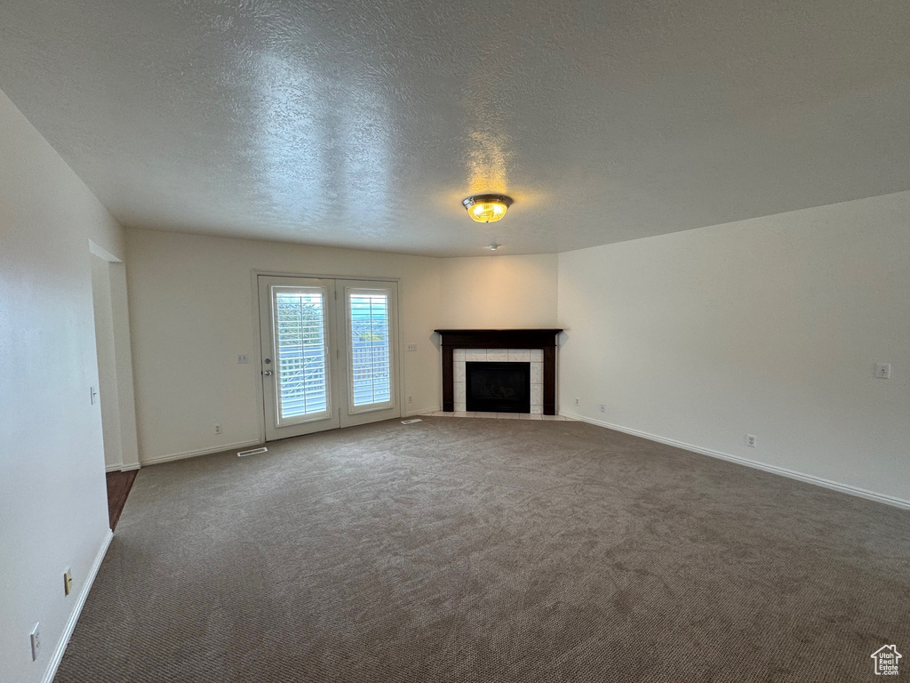 Unfurnished living room with carpet, a textured ceiling, a tiled fireplace, and baseboards