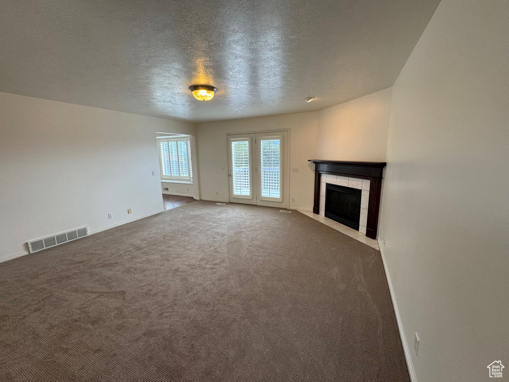 Unfurnished living room with a fireplace, a textured ceiling, carpet floors, and baseboards
