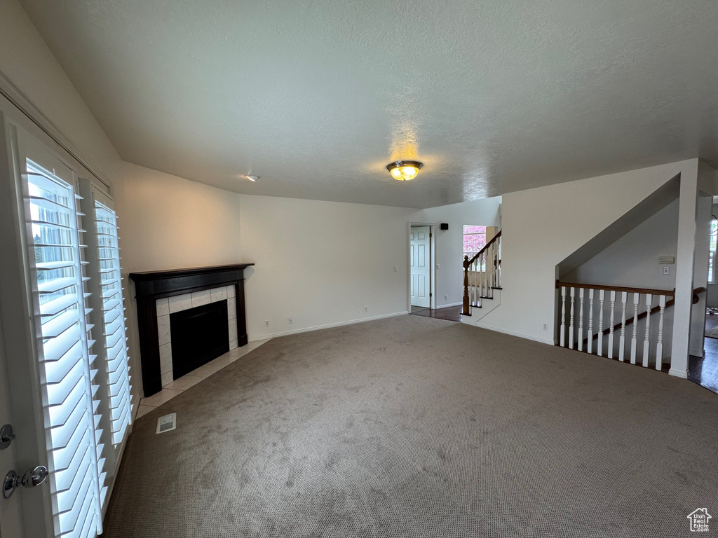 Unfurnished living room featuring carpet flooring, a tile fireplace, stairway, and baseboards