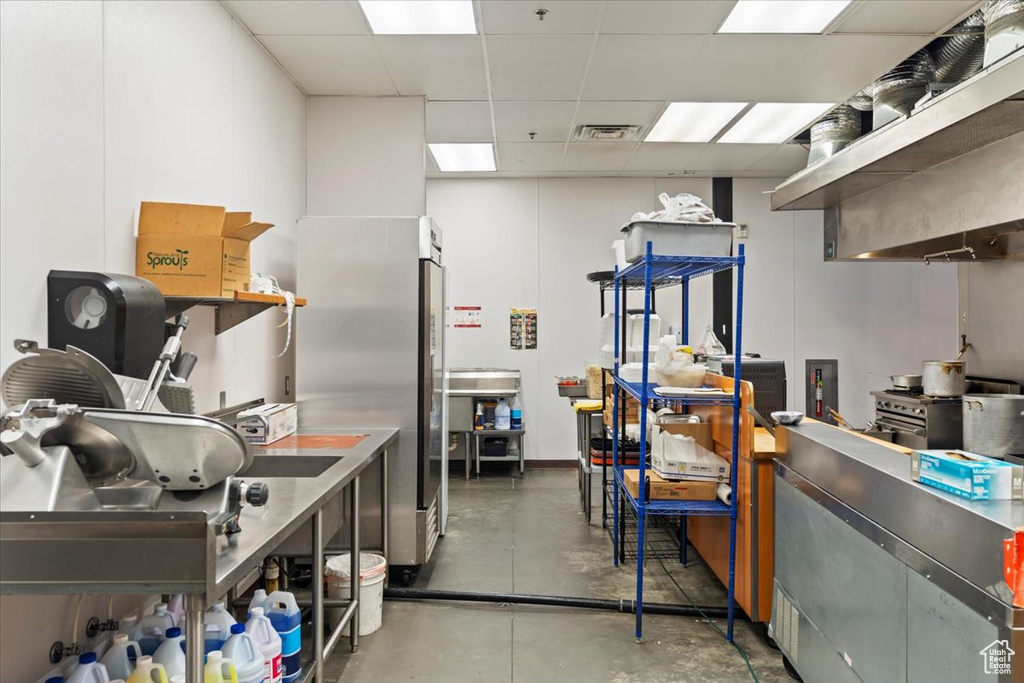 Kitchen with finished concrete flooring, visible vents, a drop ceiling, and freestanding refrigerator