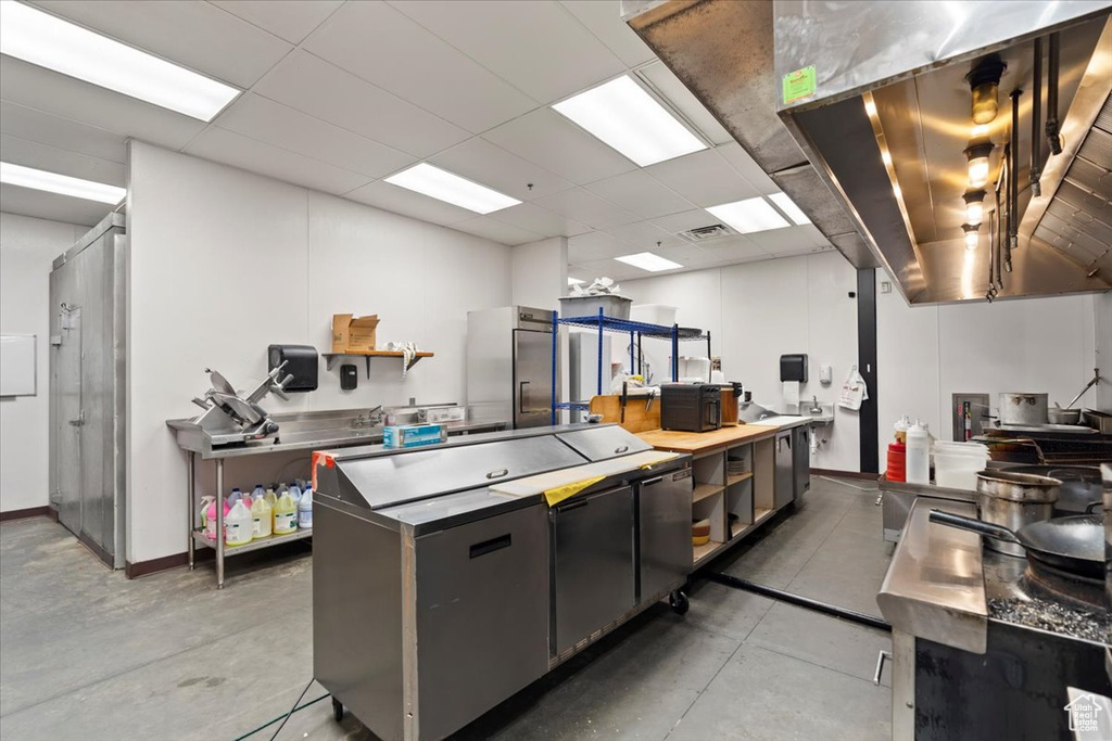 Kitchen featuring concrete floors, a drop ceiling, a center island, and dark cabinets