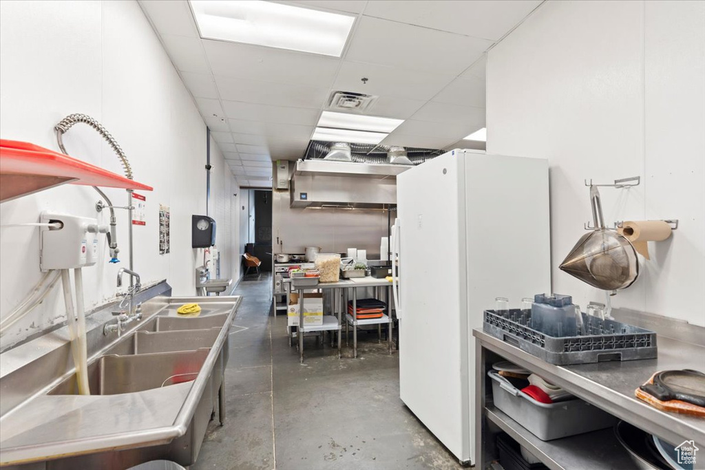 Kitchen featuring concrete flooring, a paneled ceiling, a sink, and freestanding refrigerator