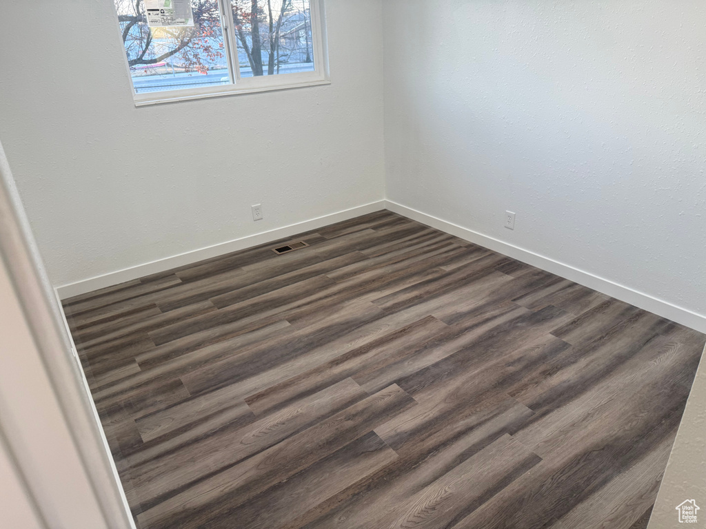 Unfurnished room with dark wood-style flooring, visible vents, and baseboards