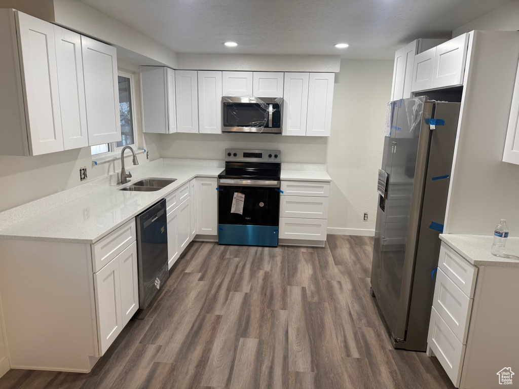 Kitchen featuring dark wood-style floors, appliances with stainless steel finishes, a sink, and white cabinetry