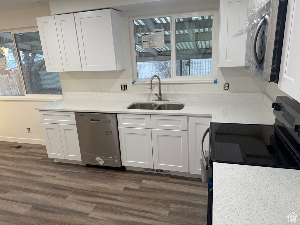Kitchen with dark wood finished floors, appliances with stainless steel finishes, light countertops, white cabinetry, and a sink