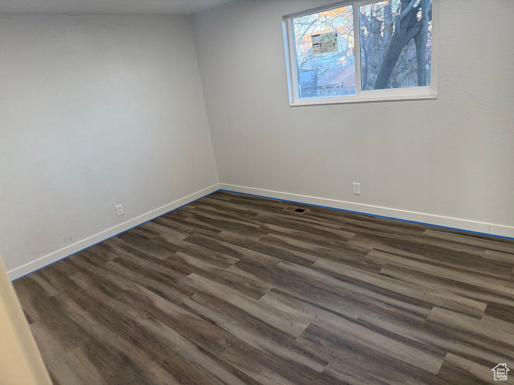 Empty room with dark wood-style floors, visible vents, and baseboards