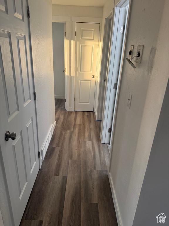 Hall featuring dark wood-style floors, visible vents, a textured wall, and baseboards