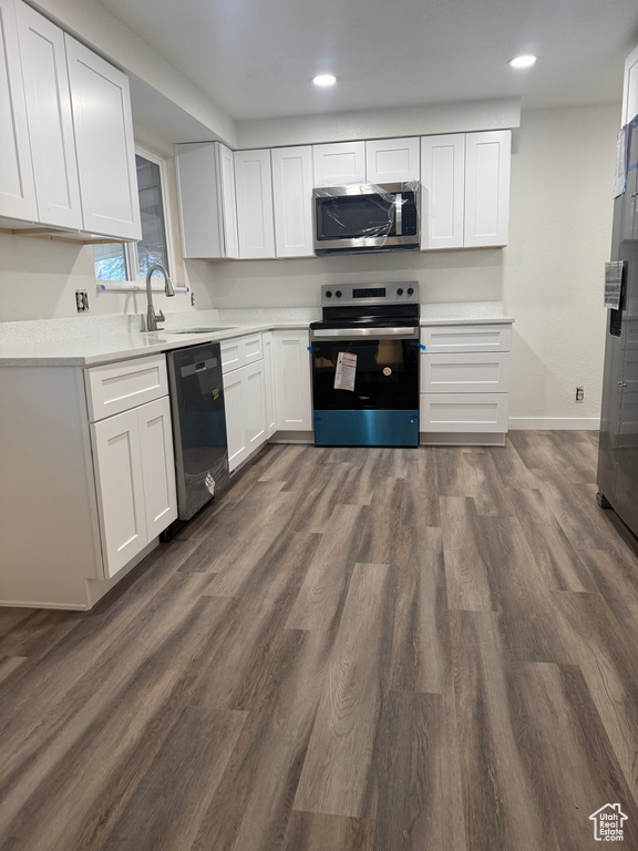 Kitchen with light countertops, appliances with stainless steel finishes, dark wood-type flooring, white cabinetry, and a sink