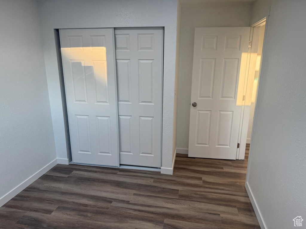 Unfurnished bedroom featuring dark wood-style flooring, a closet, and baseboards