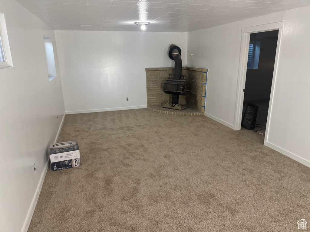 Unfurnished living room featuring a wood stove, baseboards, and carpet flooring