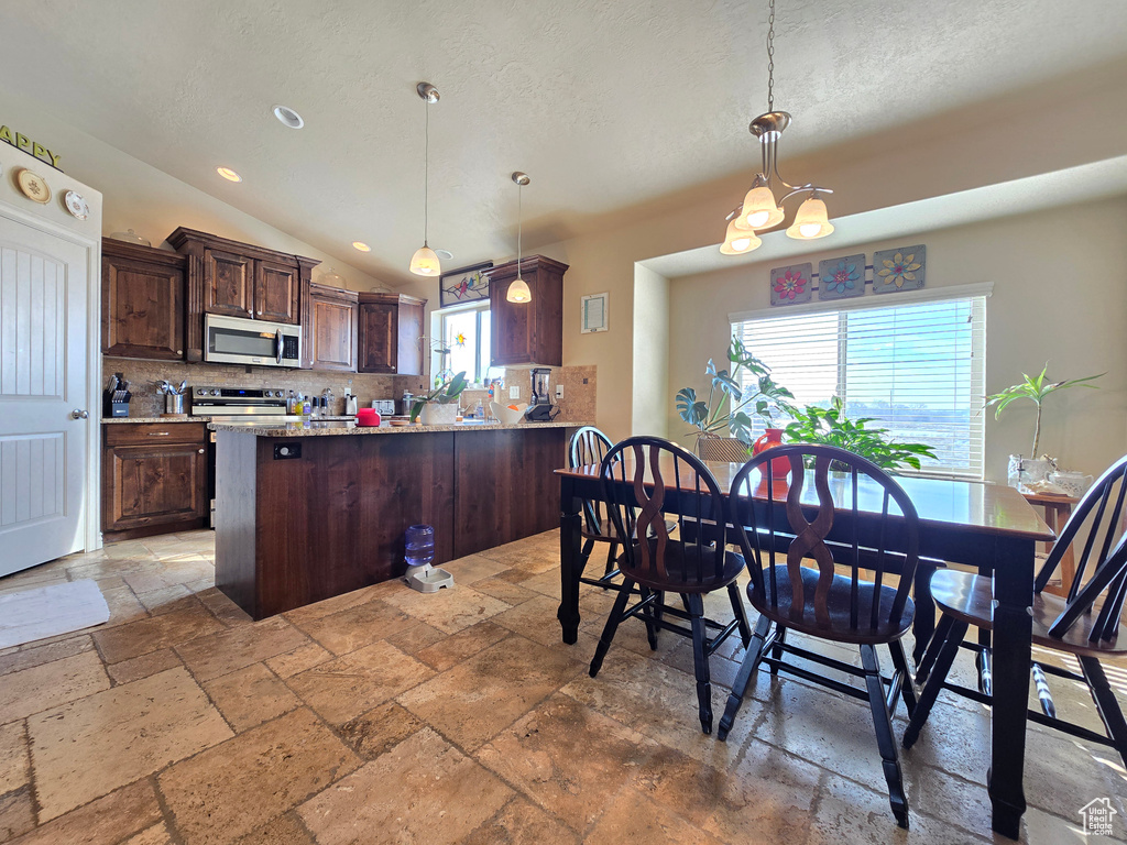 Kitchen featuring stainless steel appliances, hanging light fixtures, a peninsula, and stone tile flooring
