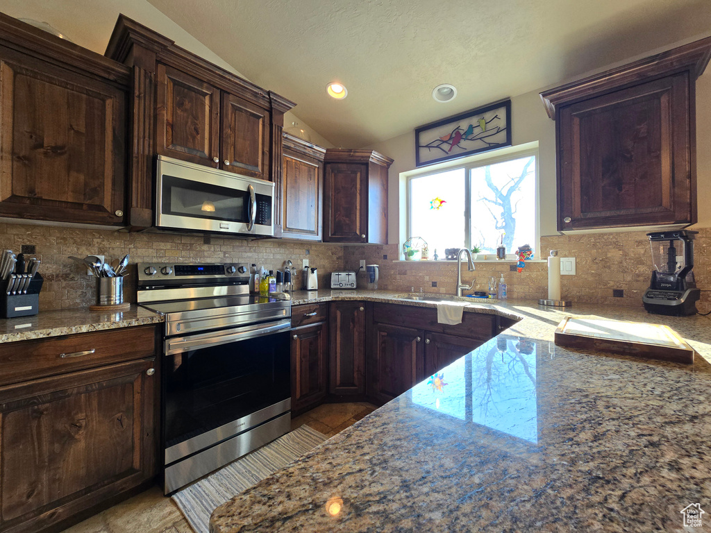 Kitchen with appliances with stainless steel finishes, a sink, vaulted ceiling, and light stone counters